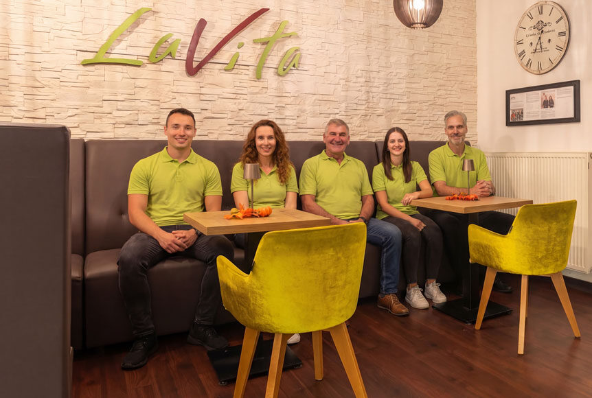 Mitarbeiter im La Vita Fitnessstudio in grünen Poloshirts, entspannt bei Gemeinschaftsaktivitäten.